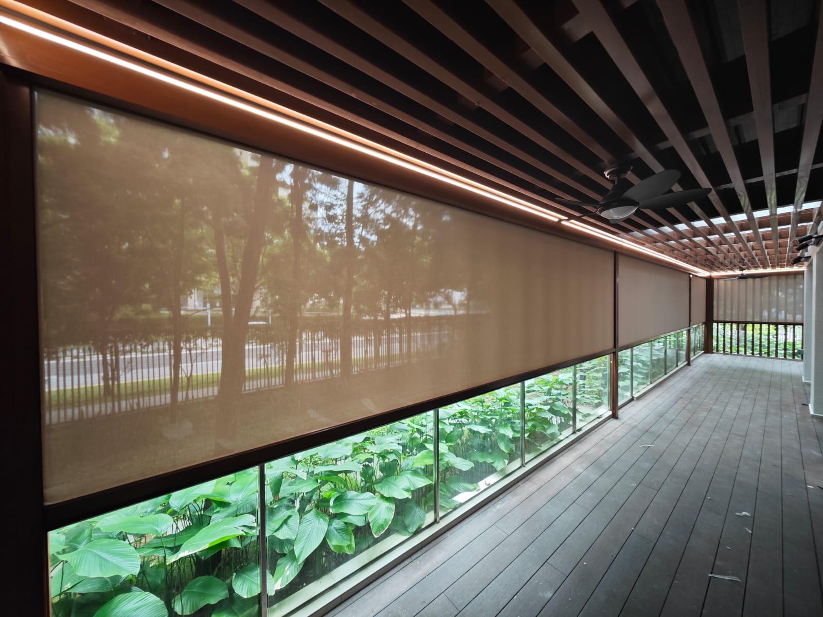 SmartZip outdoor blinds lowered along a covered balcony with greenery visible beyond the screen fabric.